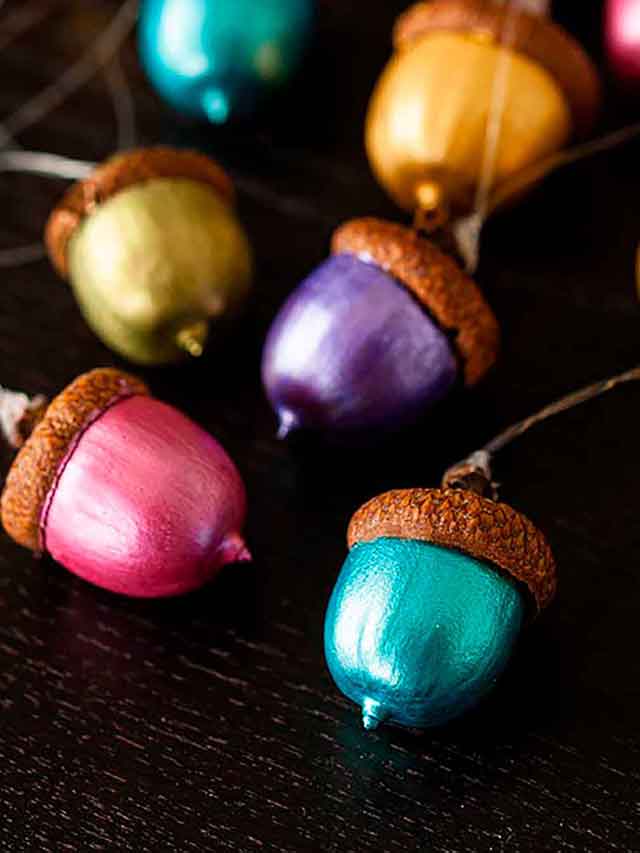 5 painted acorn ornaments on a table, in different colors.