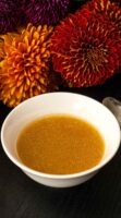 A bowl of apple cider vinaigrette in front of flowers on a table.