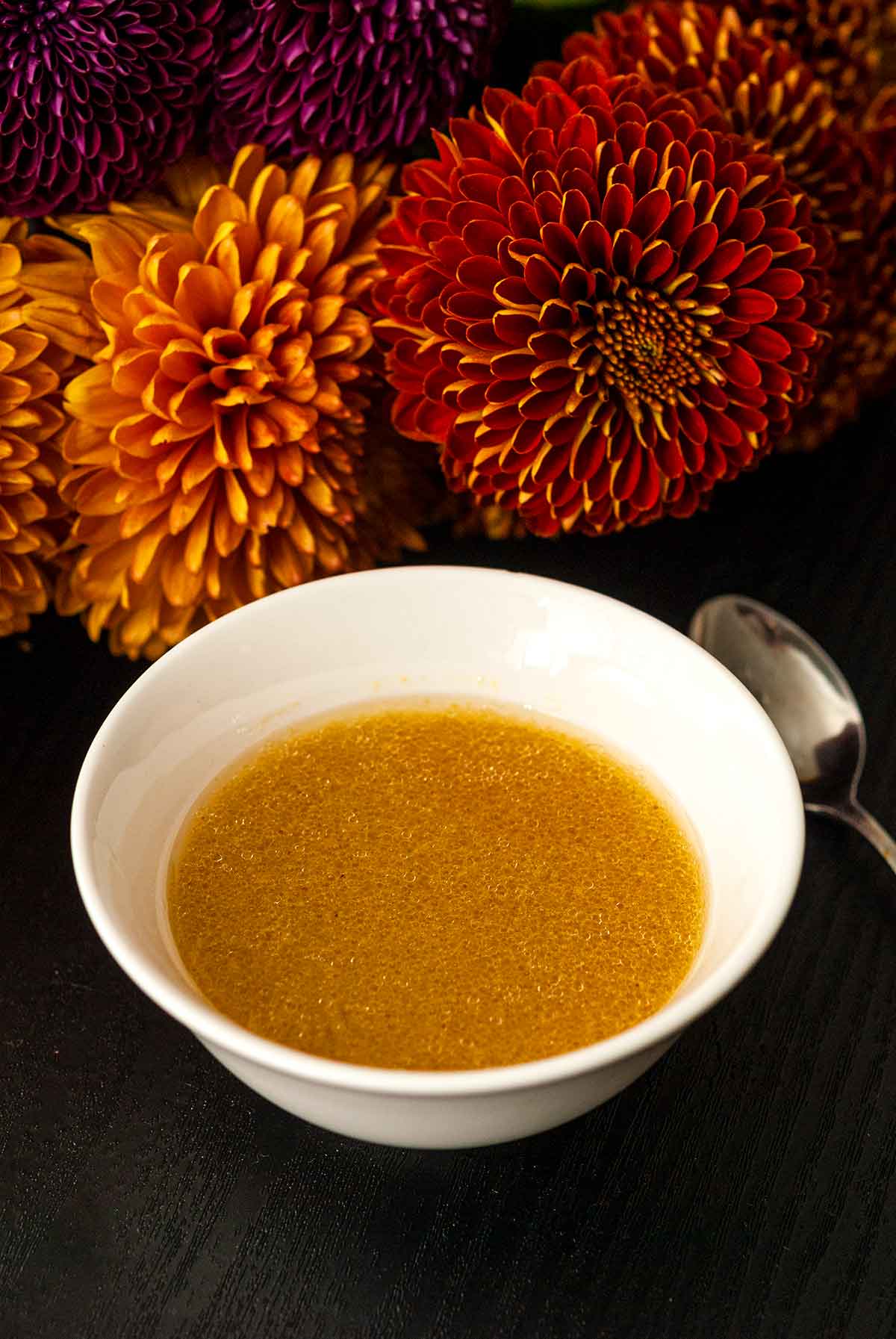 A bowl of apple cider vinaigrette in front of flowers on a table.