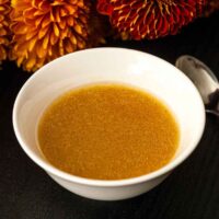 A bowl of apple cider vinaigrette in front of flowers on a table.