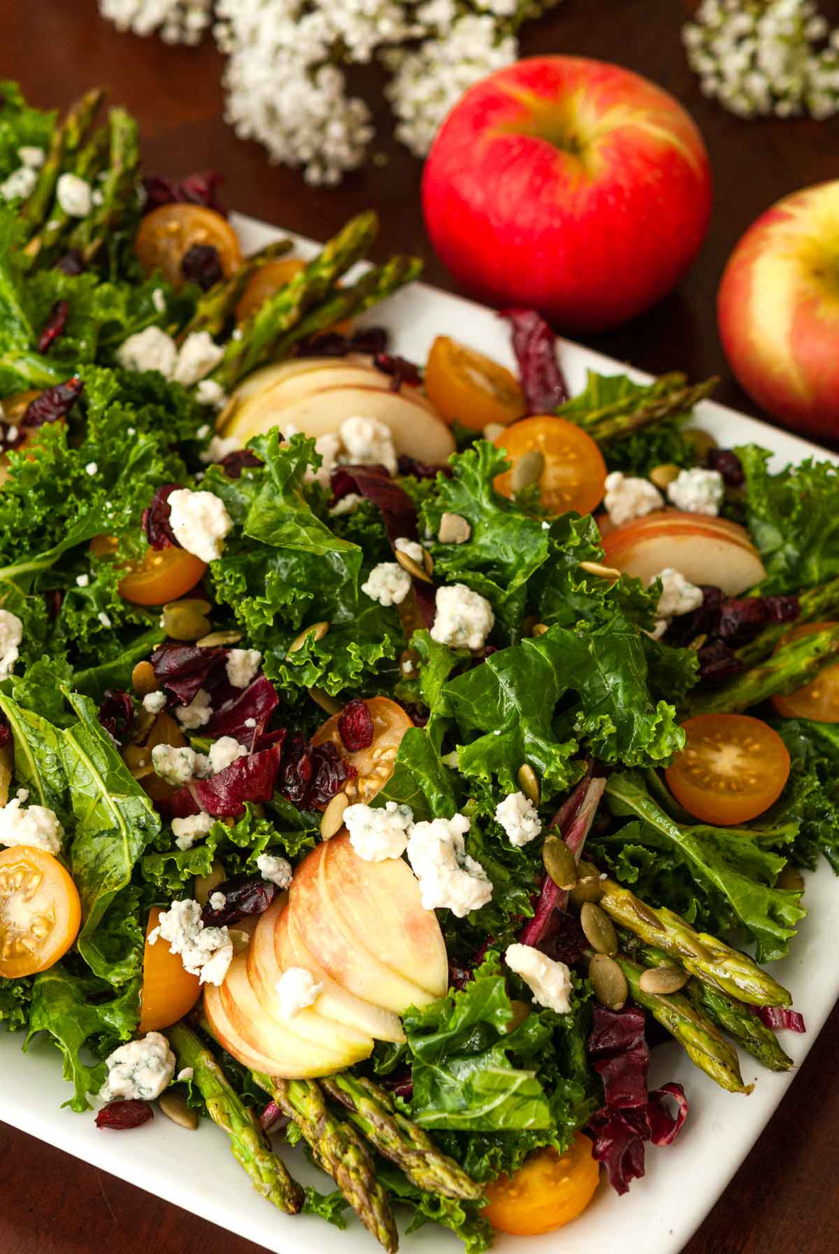 The fruits and vegetables in a specked salad in front of 2 apples.