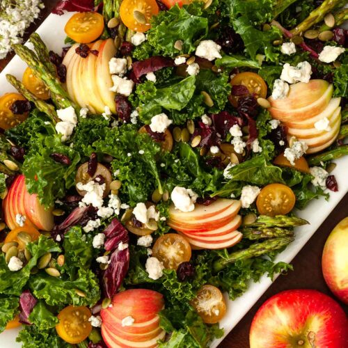 The top of an apple salad beside 2 apples on a table.