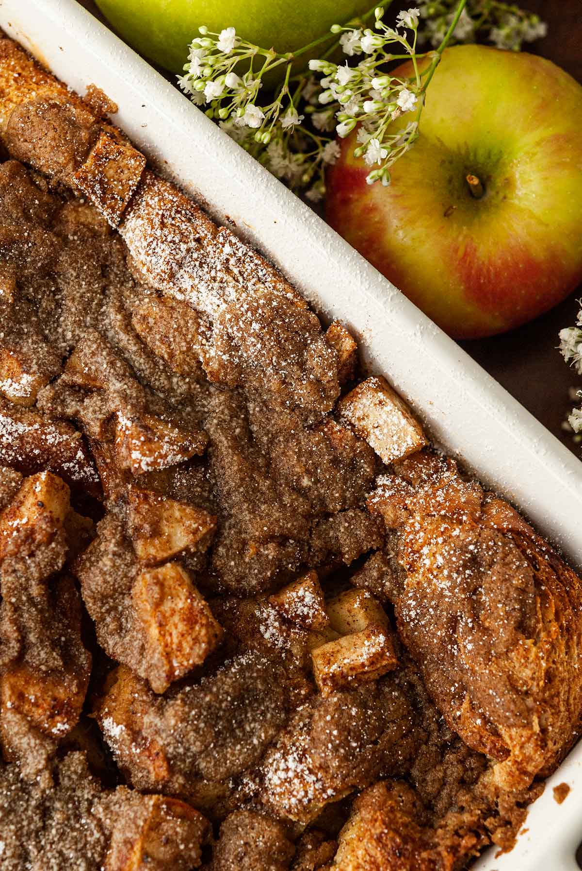 The top of a powdered french toast beside an apple and flowers.