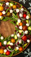 A flamboyantly garnished salad on a table in the shape of a wreath with a few scattered Christmas decorations.