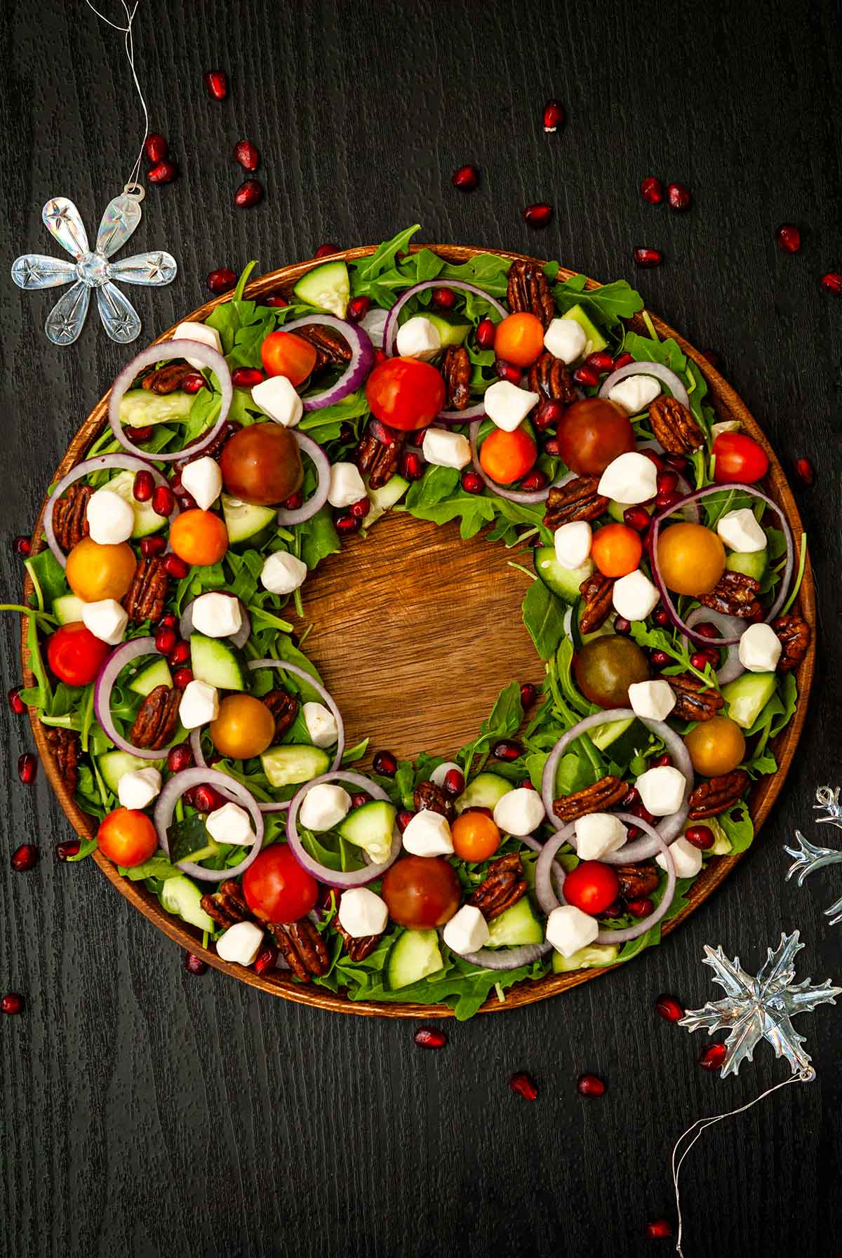 A flamboyantly garnished salad on a table in the shape of a wreath with a few scattered Christmas decorations.