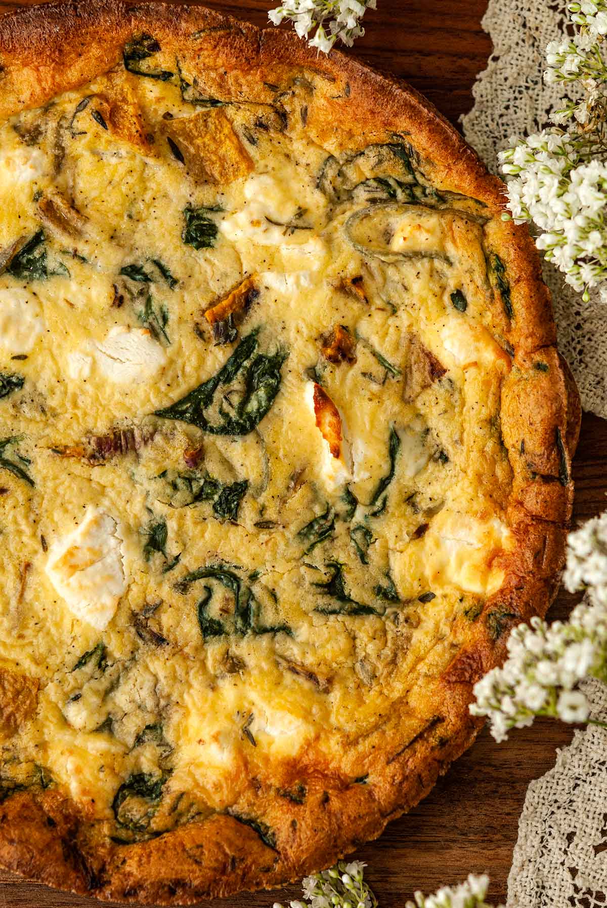 A butternut squash goat cheese quiche surrounded by flowers and lace.