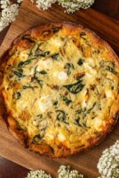 A butternut squash goat cheese quiche on a wooden board, surrounded by flowers.