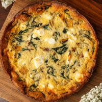 A butternut squash goat cheese quiche on a wooden board, surrounded by flowers.