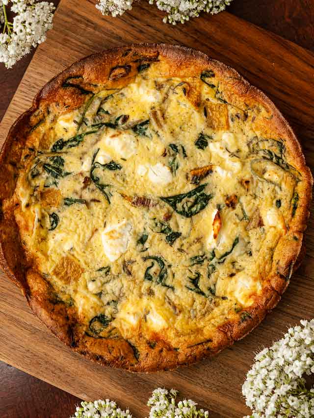A butternut squash goat cheese quiche on a wooden board, surrounded by flowers.