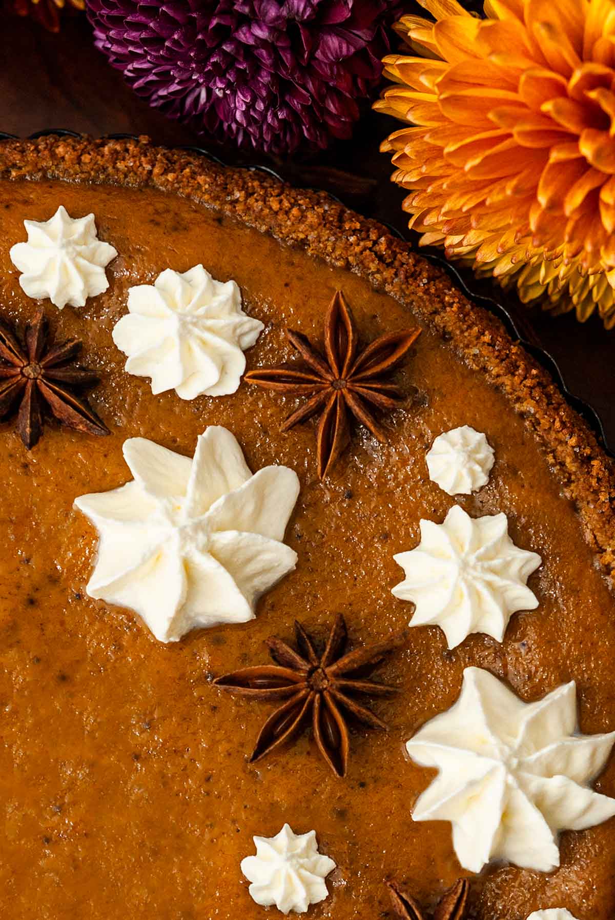 Whipped cream stars and star anise on a masala chai pumpkin pie beside flowers.