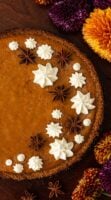 A masala chai pumpkin pie decorated with whipped cream stars and star anise beside flowers on a table.