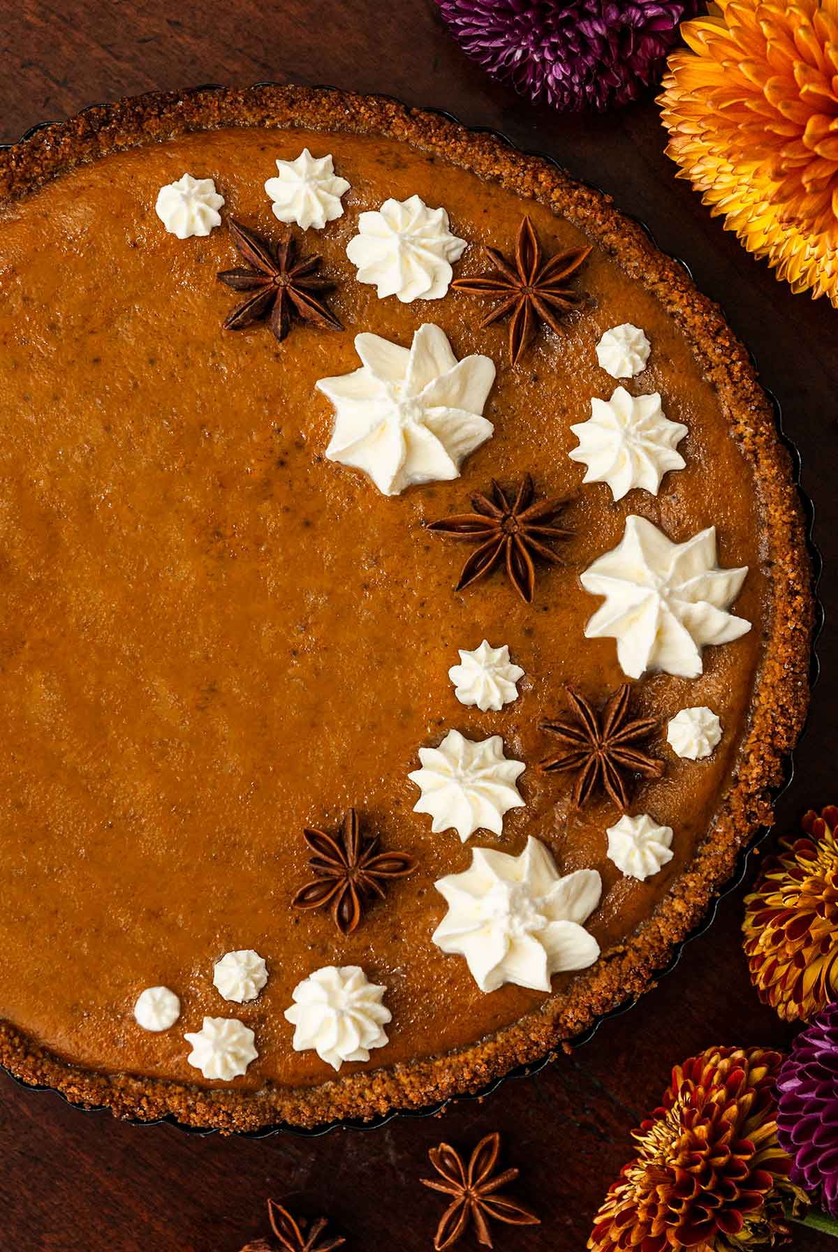 A masala chai pumpkin pie decorated with whipped cream stars and star anise beside flowers on a table.