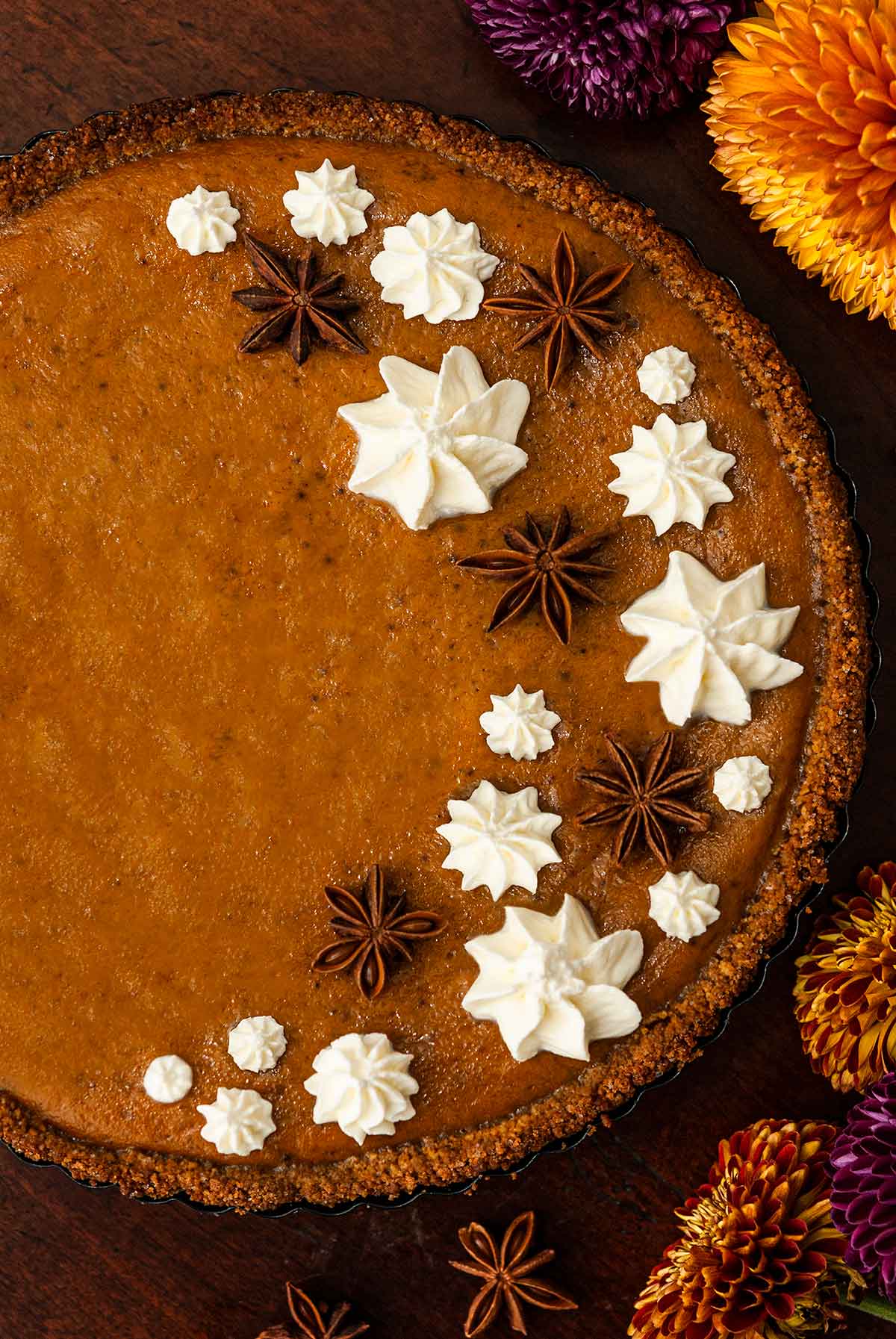 A masala chai pumpkin pie decorated with whipped cream stars and star anise beside flowers on a table.