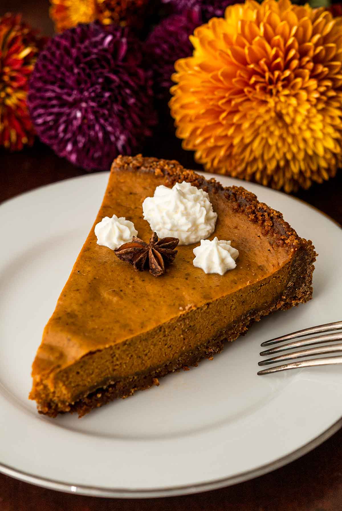 A slice of masala chai pumpkin pie topped with whipped cream and star anise beside flowers.