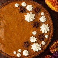 A masala chai pumpkin pie decorated with whipped cream stars and star anise beside flowers on a table.