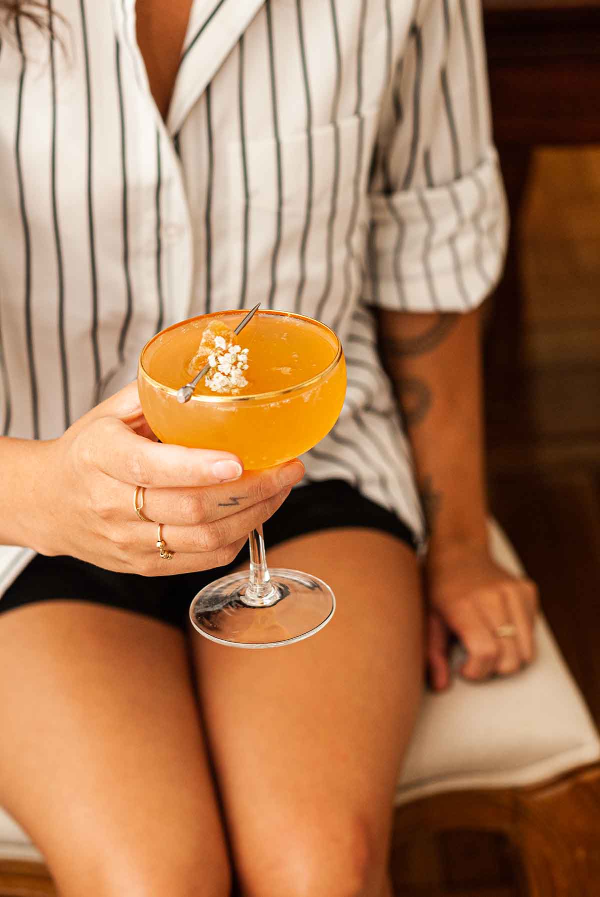A garnished mulled ginger apple cider mimosa in the hand of a woman sitting on a chair.