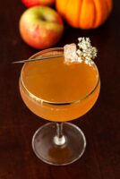 A garnished mulled ginger apple cider mimosa on a table in front of apples and a small pumpkin.