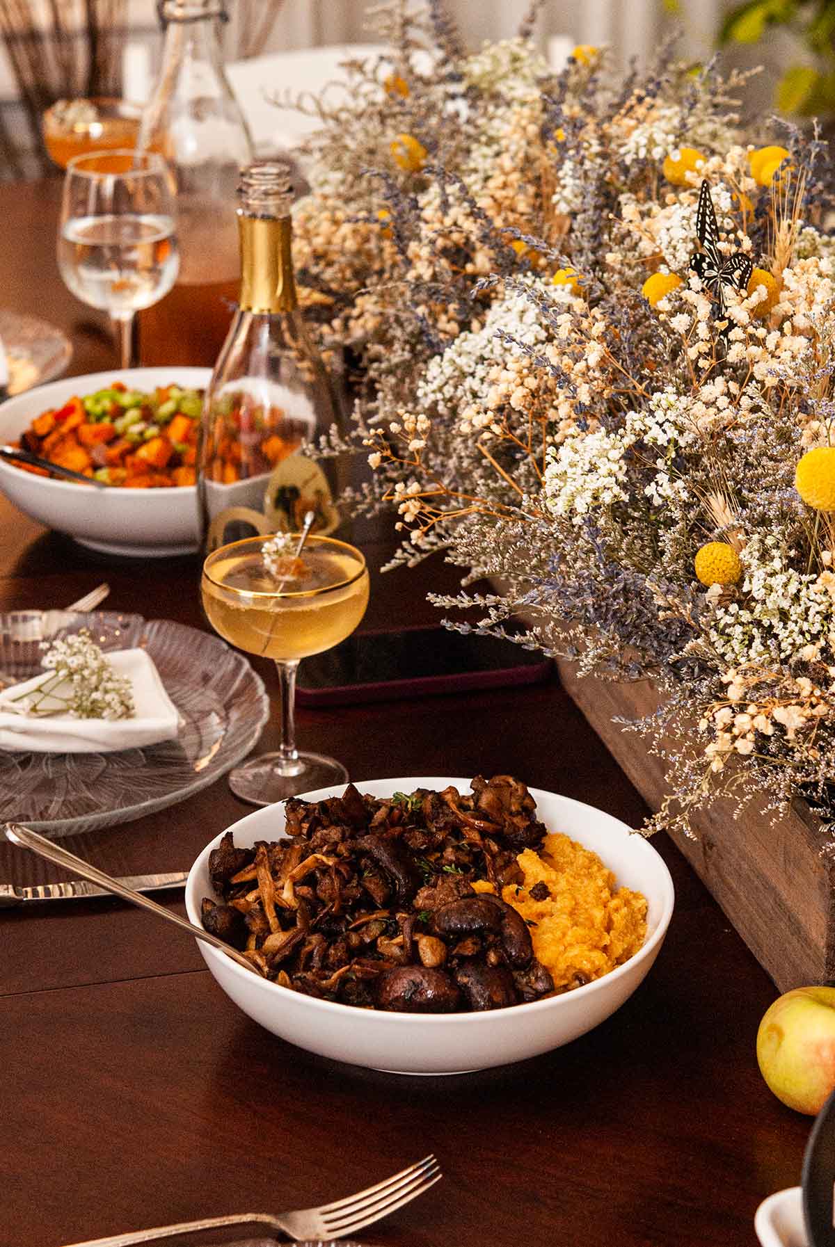 A table with an elaborate dry flower arrangement with bowls of food and cocktails.