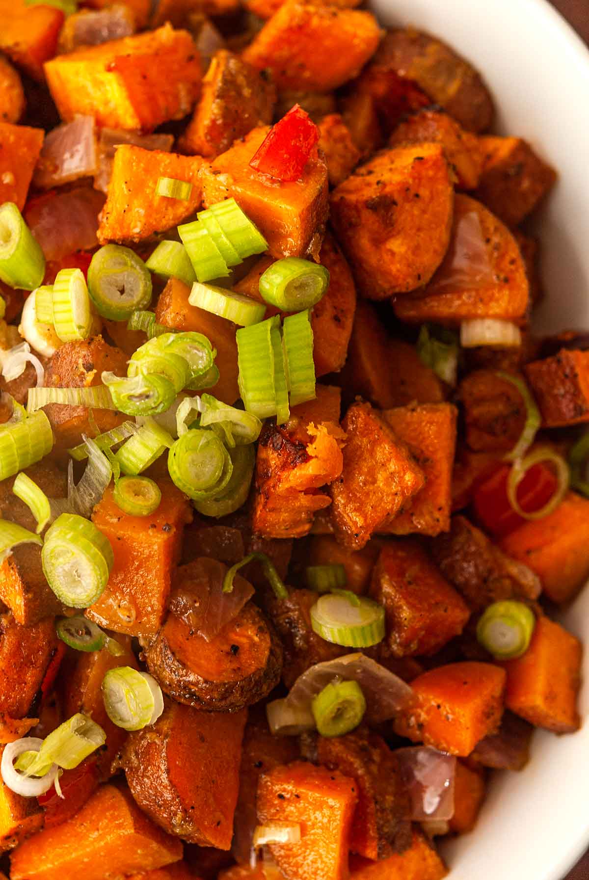 The scallions on top of a bowl of sweet potato hash.