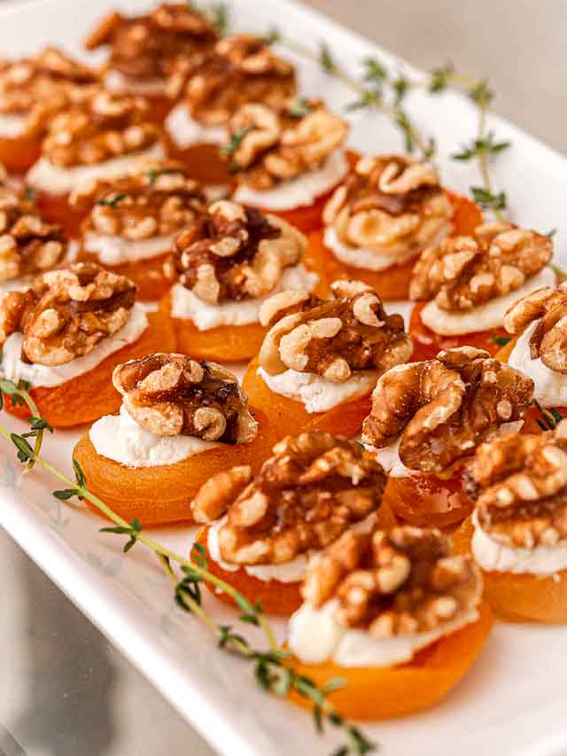 About 20 apricot appetizers on a plate, garnished with thyme.