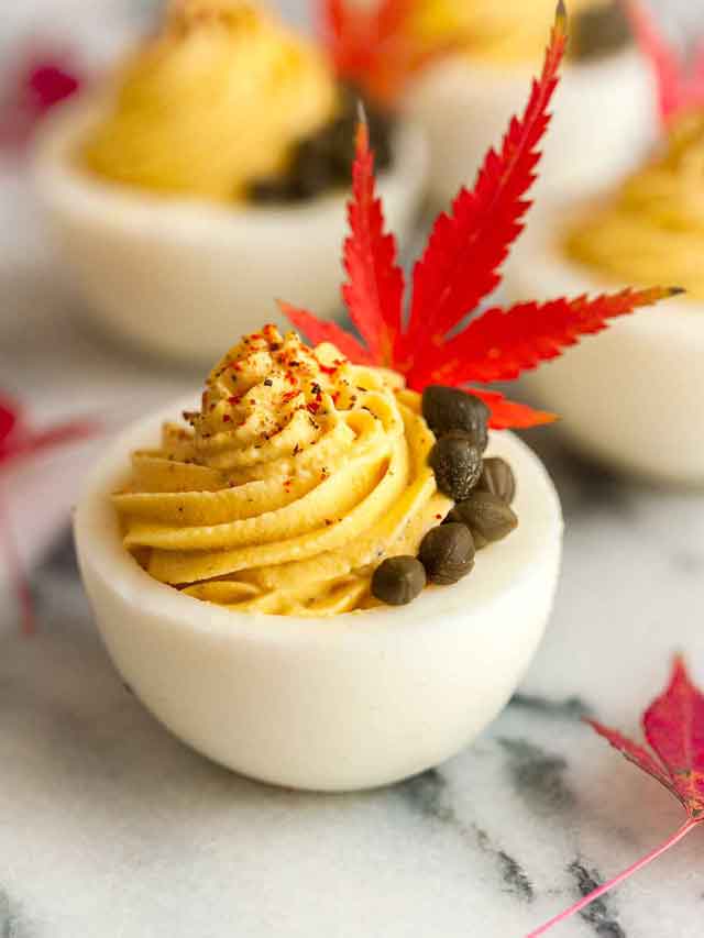 A deviled egg garnished with a maple leaf and capers on marble.