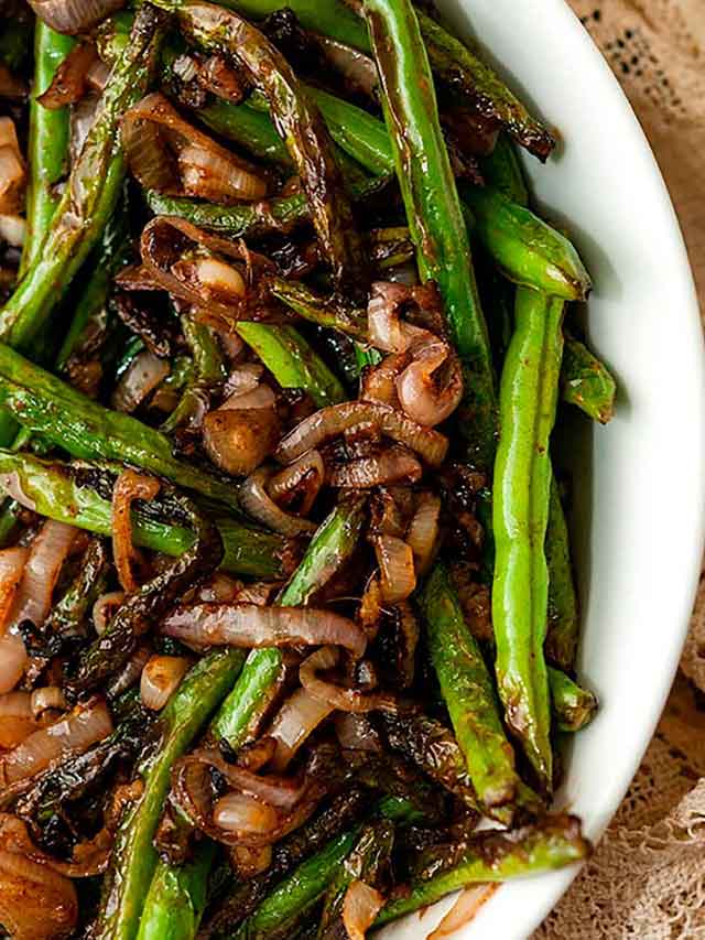 A bowl of green beans with sautéed shallots.