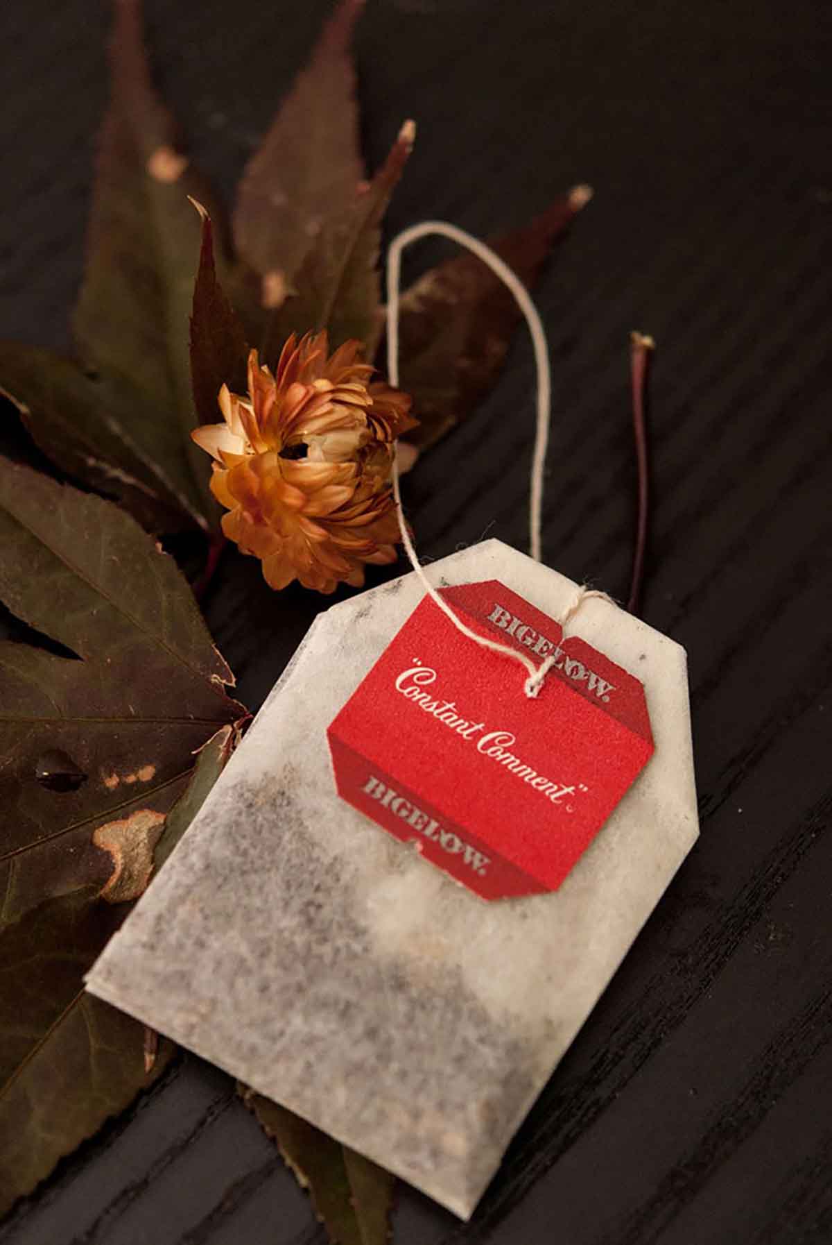 A Constant Comment tea bag on a table with dry flowers and leaves.