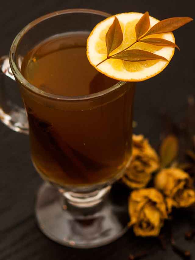 A hot toddy, garnished with an orange slice and leaf with 3 dry roses beside it.