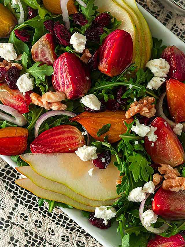 A salad with colorful vegetables, pears, berries and nuts on a lace table cloth.