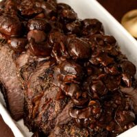 Top round roast beef in a tray with mushroom sauce.