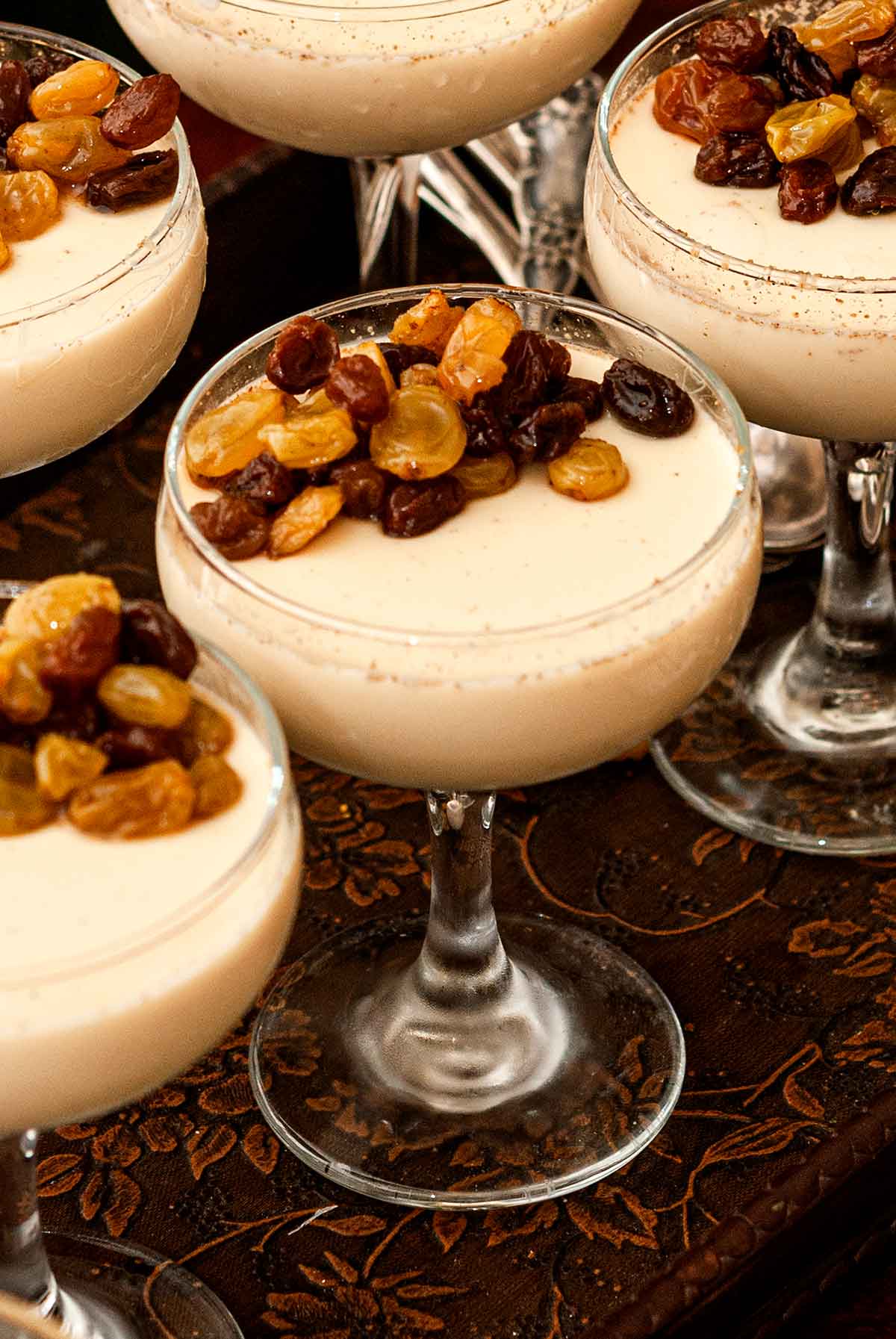 5 chai-spiced eggnog panna cottas with raisins on a serving tray.