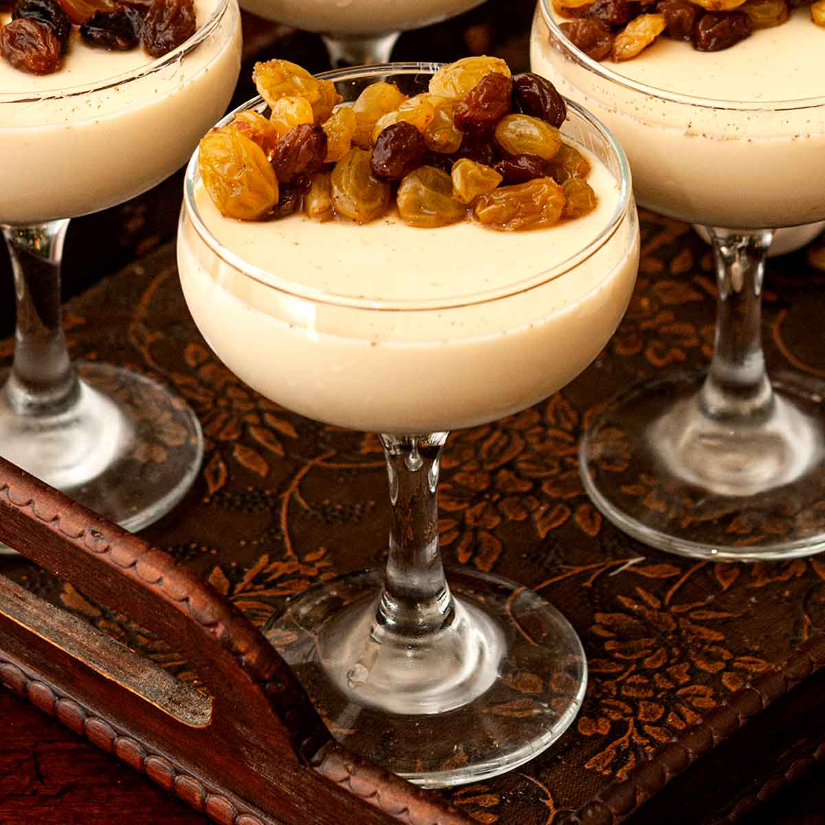 3 chai-spiced eggnog panna cottas with raisins on a serving tray.