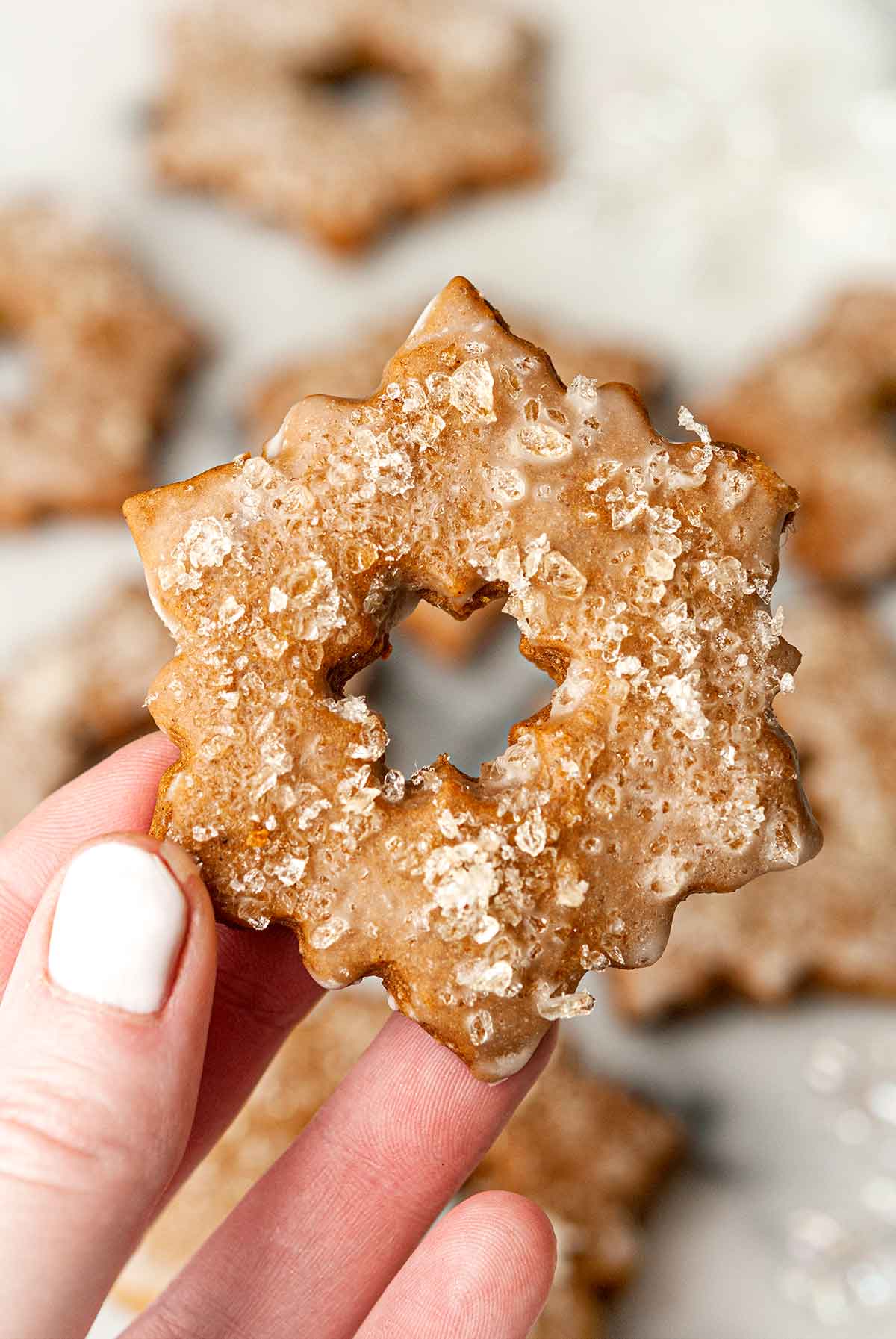 Fingers holding a glazed, sugared gingerbread cookie.