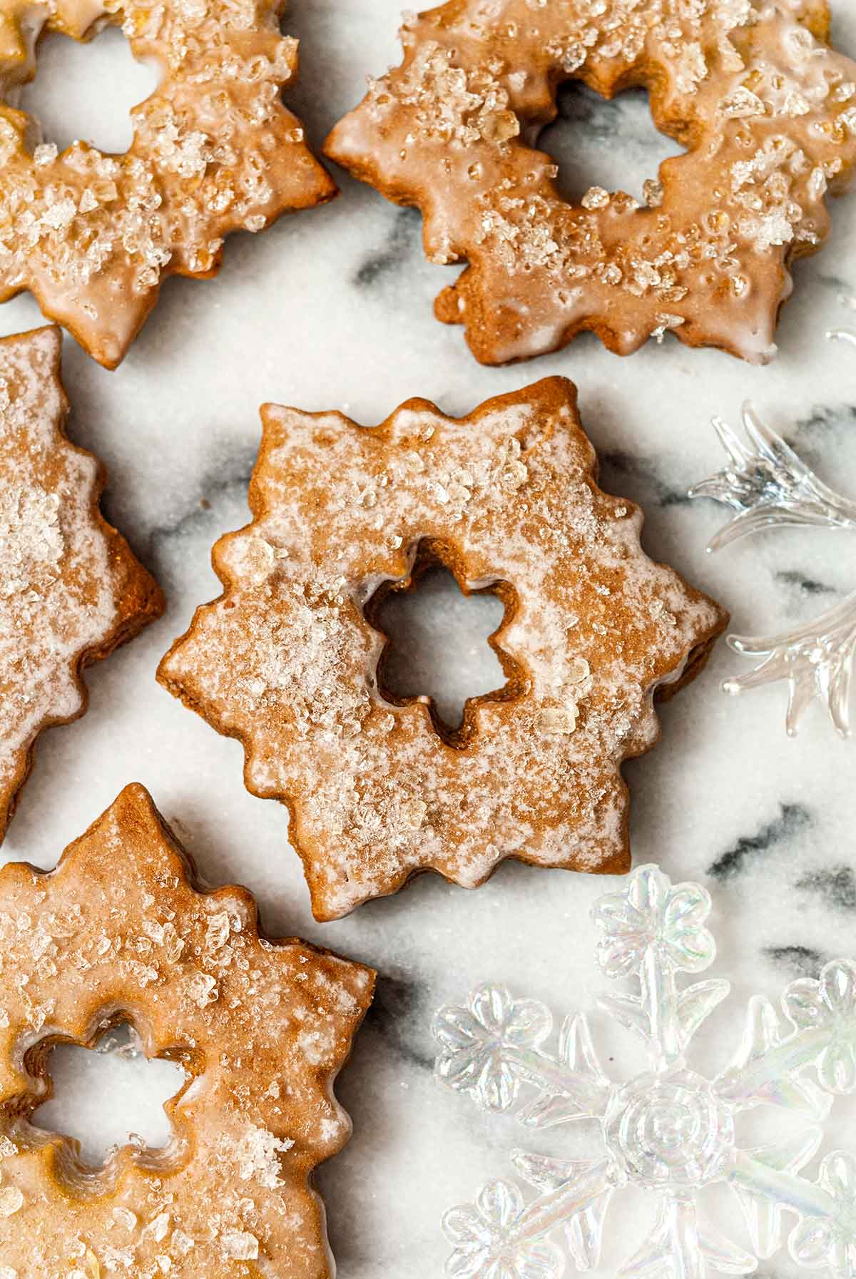 5 glazed, sugared gingerbread cookies on marble with glass ornaments.