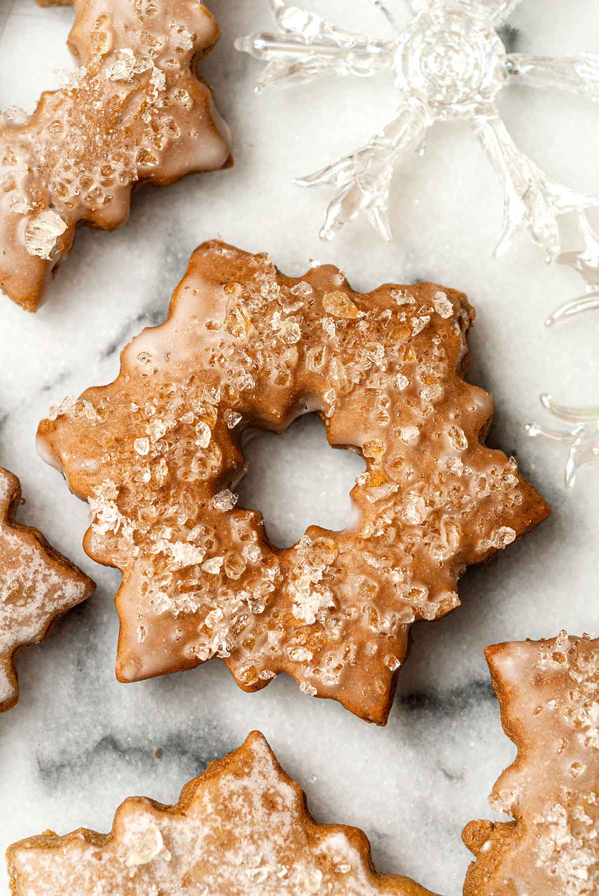 5 glazed, sugared gingerbread cookies on marble with glass ornaments.