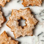 A glazed, sugared Christmas cookie on marble beside glass ornaments.