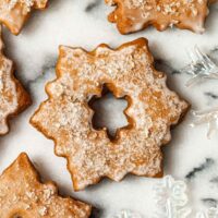 A glazed, sugared Christmas cookie on marble beside glass ornaments.