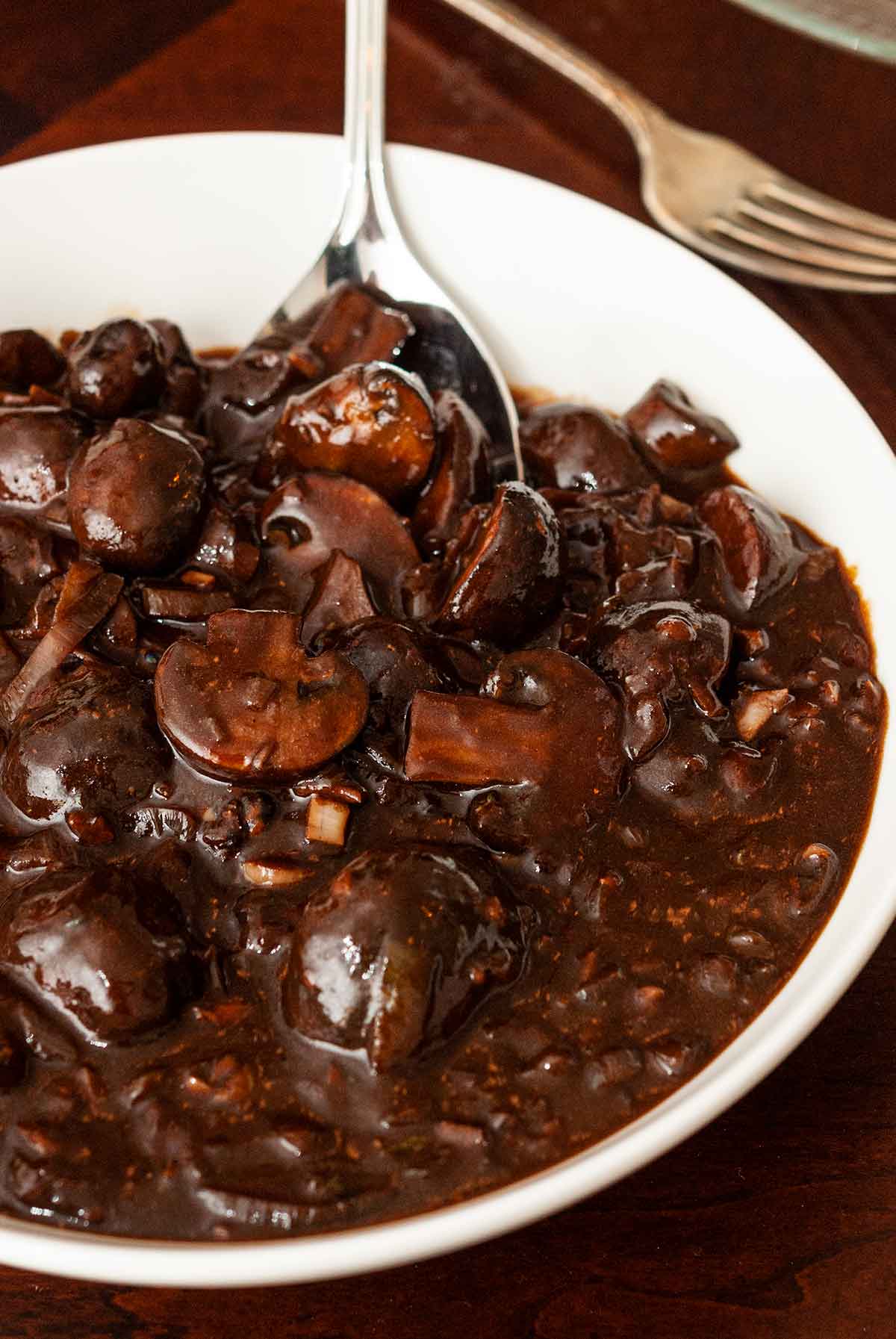 A bowl of red wine mushrooms sauce with a spoon on a table.