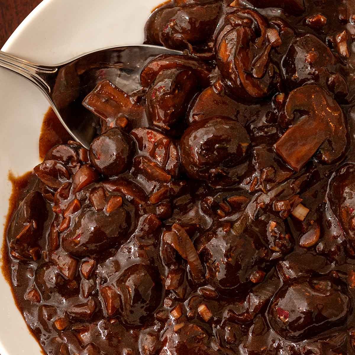 A bowl of red wine mushrooms sauce with a spoon,