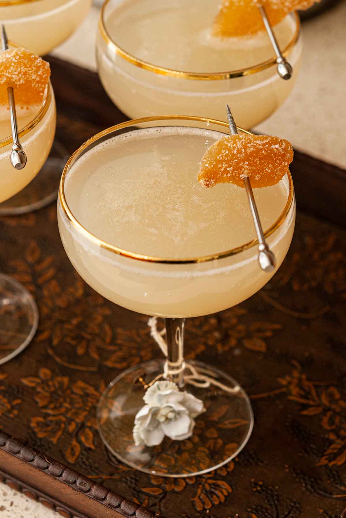 4 cocktails on a tray, garnished with candied ginger, and glass charms.