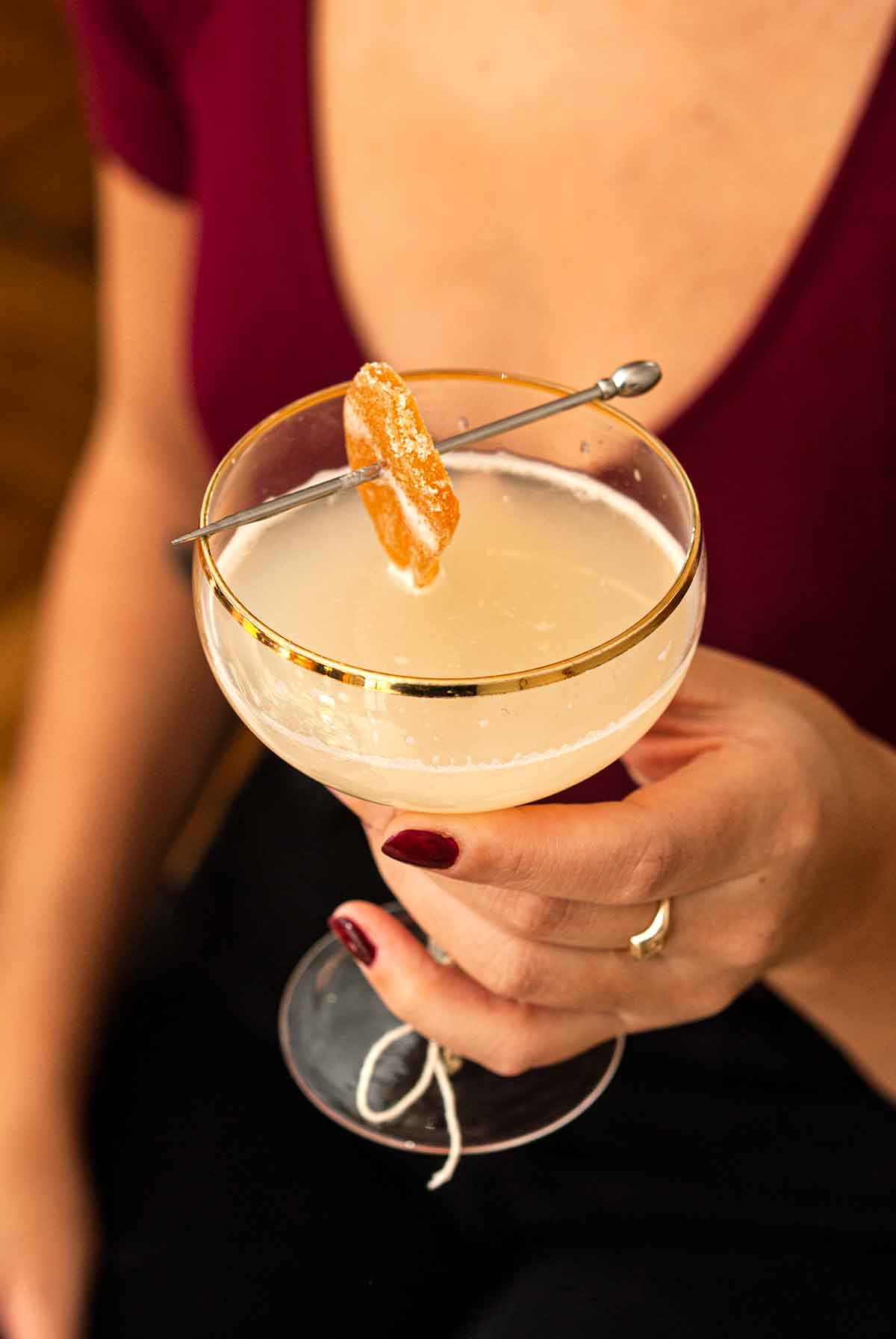 A woman's hand holding a cocktail garnished with candied ginger.