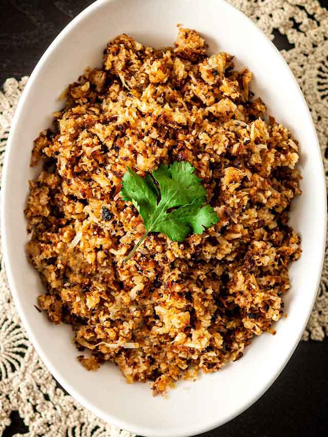 Coconut cauliflower rice in a bowl, topped with a cilantro leaf, on a table with lace.
