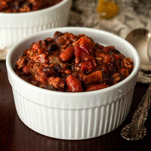 A bowl of chili on a table beside a spoon.