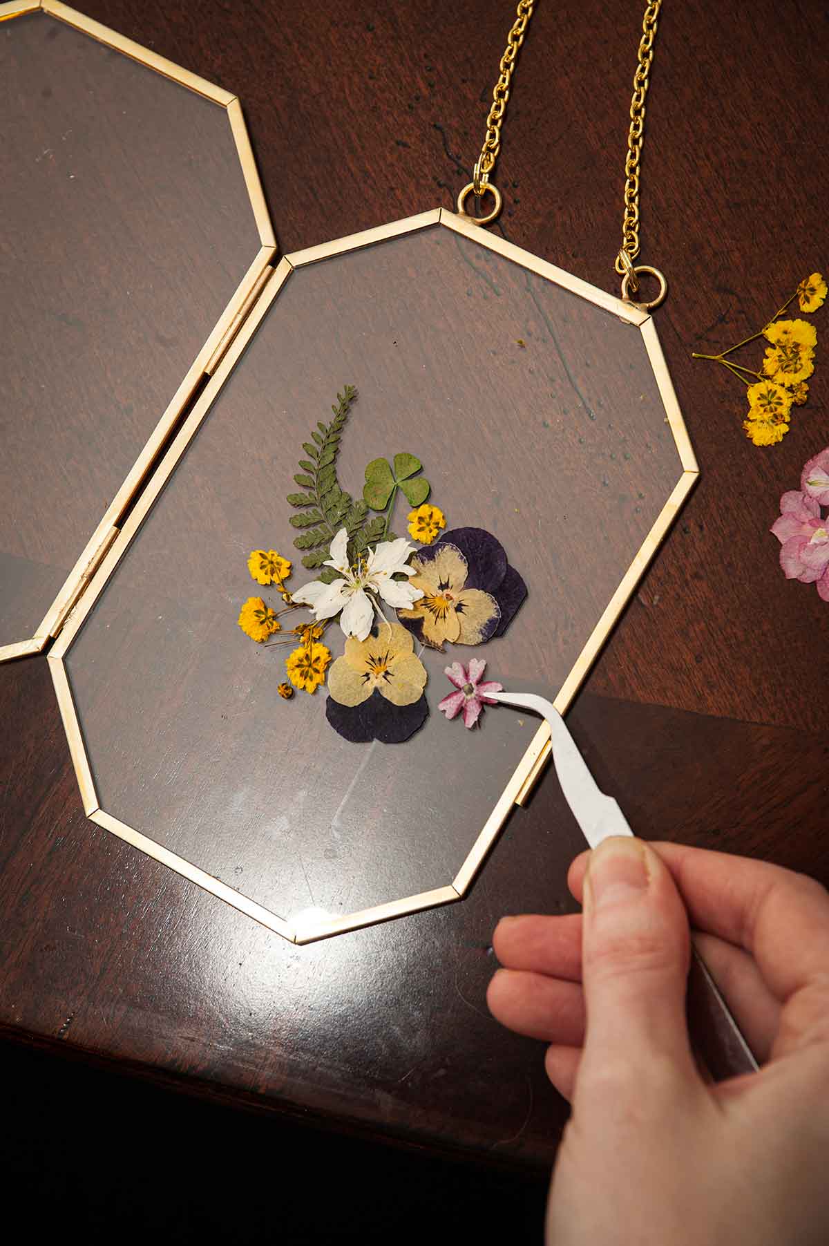 Fingers using tweezers to place flowers on a clear frame.