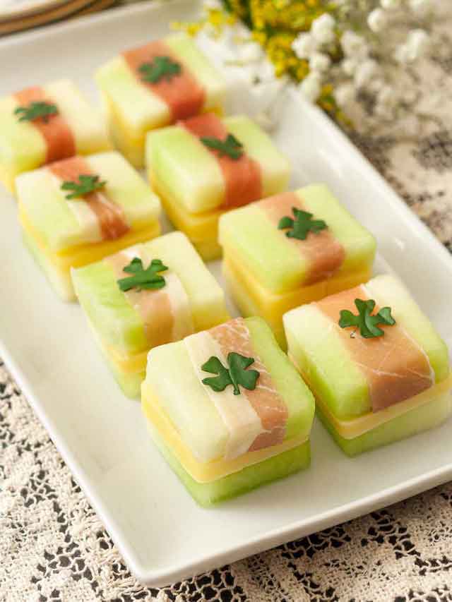 8 melon, cheese and prosciutto appetizers with basil clovers on a plate.