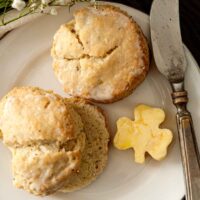 2 scones on a plate beside shamrock-shaped butter and a knife.