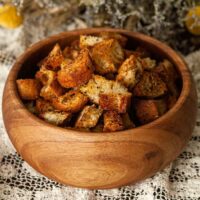 A bowl of Italian croutons on a lace table cloth in front of flowers.