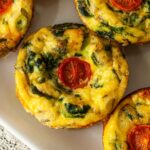 A mini-quiche on a plate topped with a tomato.