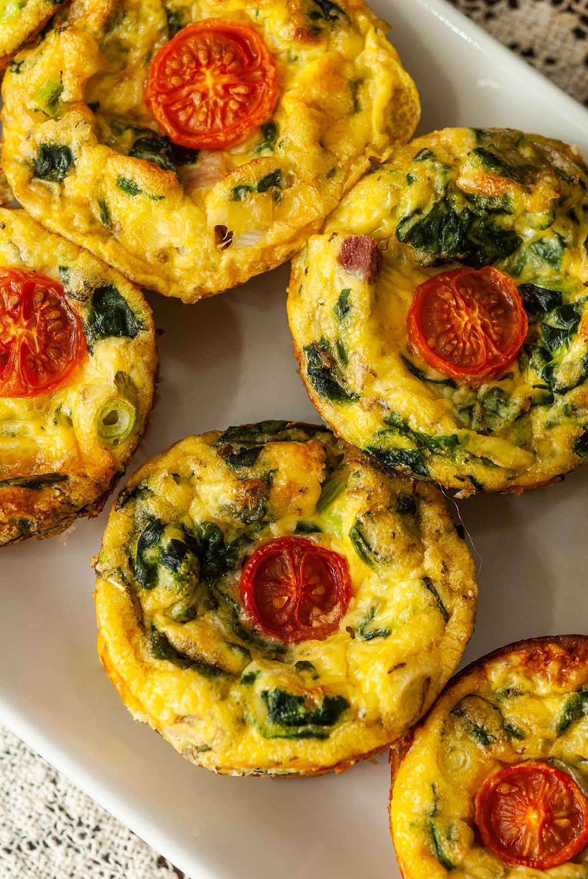 5 mini-quiches on a plate topped with tomatoes.