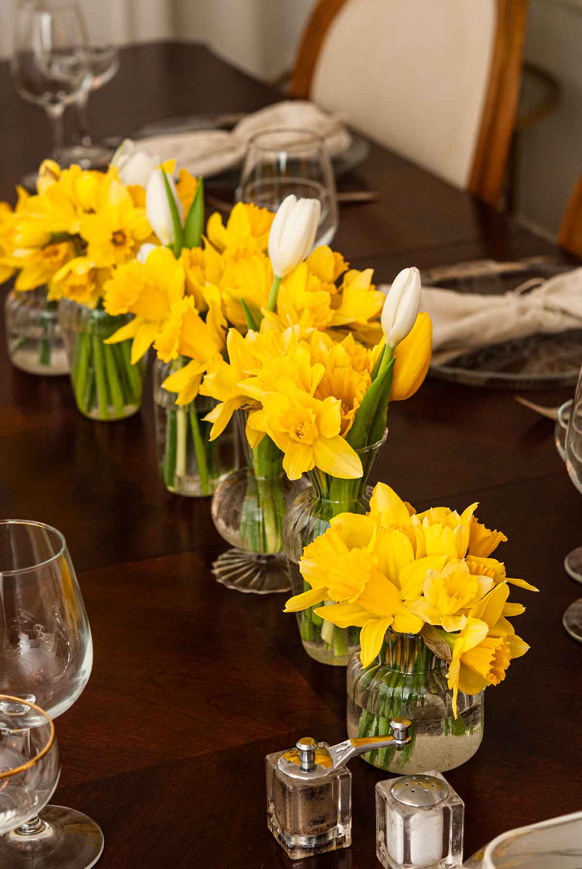 A row of daffodils in glass vases on a diner table.